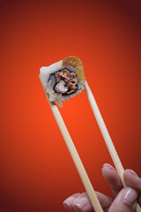 Close-up shot of chopsticks holding a single piece of sushi roll against a warm orange background © hcarbuccia