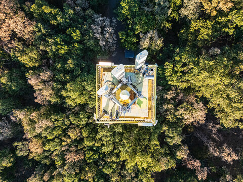 Aerial view of telecommunications antennas on a tower observation deck rising above dense late-summer forest canopy in Sasto, Hungary, in the Matra Mountains.