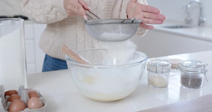 Home cook is tapping sieve to sift flour into bowl at kitchen island following tablet recipe