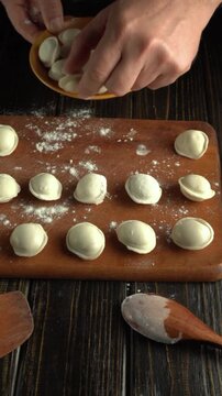 Hands arrange small round dumplings on a floured wooden board beside a bowl and flour dusted utensils during homemade food preparation