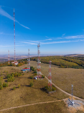 Aerial view of Feleacu 311A Cluj telecommunication towers standing on a grassy hill with autumn foliage and a clear blue sky in Cluj-Napoca, Judetul Cluj, Romania.