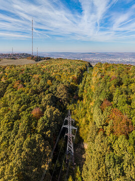 Aerial view of the Feleacu TV tower and power transmission lines cutting through a dense, autumn-colored forest in the hills overlooking Cluj-Napoca, Judetul Cluj, Romania.