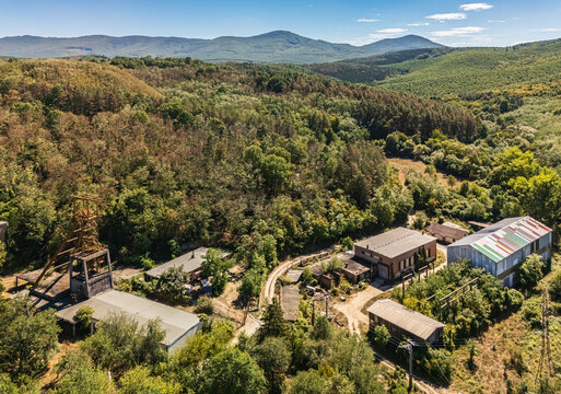 Aerial view of the abandoned Tiribesi-Akna coal mine buildings and headframe surrounded by forested Matra hills near Batonyterenye, Hungary, in summer.