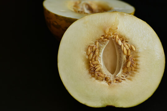 Two half yellow melon on black background. Sweet organic melon cut of half with seeds. Food and fruit background, Health , vitamins concept.