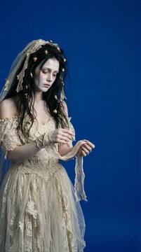 Ghost bride in a lace wedding dress unwrapping a bandage on a blue background with copy space