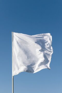 Close-up of a crisp white flag fluttering on a slim flagpole against a clear blue sky
