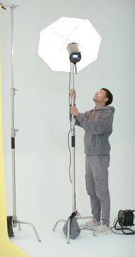 Vertical video: Man adjusting stand and umbrella with lamp powering on in studio to aim light