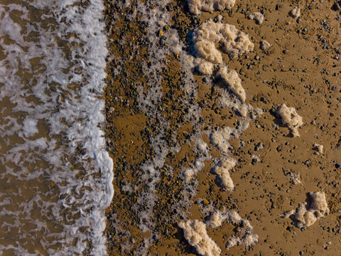 Aerial view of the shoreline with sea foam, wet sand, and pebbles at the water's edge in Talacre, Flintshire, United Kingdom.