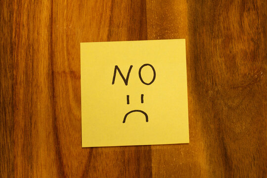 Sticky note with a sad face and the word "no" on wooden table
