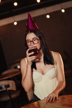 beautiful woman wearing a birthday hat, holding a beer in a bar