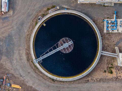 Aerial view of a circular water treatment clarifier tank with industrial piping and gravel surroundings at The Common, Queensland, Australia.