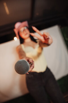 Beautiful woman wearing a cowboy hat and holding a microphone, singing at a karaoke session.