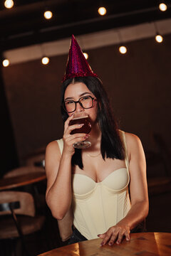 beautiful woman wearing a birthday hat, holding a beer in a bar