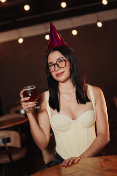 Beautiful woman wearing a birthday hat holding a beer in a karaoke bar.