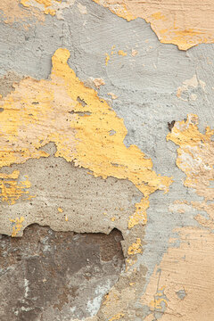 A close-up photograph of a wall with weathered, pastel-colored plaster. An old, worn-down surface featuring layers of plaster. Renovation, refurbishment, restoration