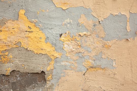 A close-up photograph of a wall with weathered, pastel-colored plaster. An old, worn-down surface featuring layers of plaster. Renovation, refurbishment, restoration