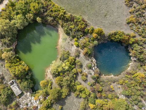 Aerial view of Hordhanat e Virit featuring two contrasting green and blue sinkhole lakes surrounded by dense autumn foliage and rocky terrain in Bajze, Shkoder County, Albania.