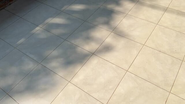Hard sunlight shadow moving across square ceramic floor tiles, geometric architectural interior backdrop