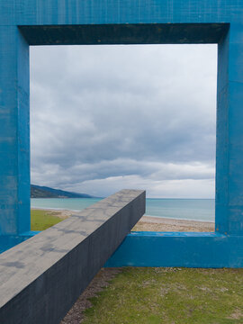 Aerial view of Monumento per un Poeta Morto framing the sea and coastline with a dark concrete beam extending through the blue structure in Villa Margi, Sicilia, Italy.