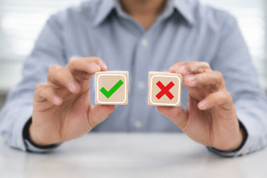 Hands presenting red cross and green check blocks symbolize right or wrong choice of decision making with approval and rejection evaluation yes or no of business judgment concept.