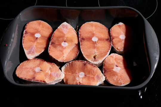 Raw pork loin chops arranged in dark roasting pan showing bone-in centers pink flesh marbling fat edges for culinary preparation and meat presentation, with pork, chop, loin, bonein detail