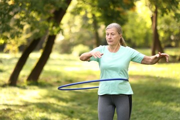 Senior woman exercising with hula hoop outdoors, space for text © New Africa