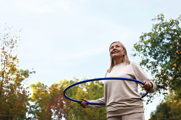 Senior woman exercising with hula hoop outdoors, low angle view. Space for text © New Africa