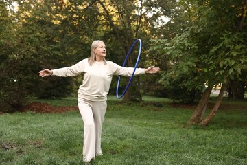 Senior woman exercising with hula hoop outdoors, space for text © New Africa