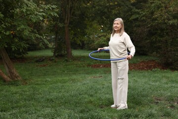 Senior woman exercising with hula hoop outdoors, space for text © New Africa