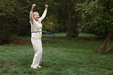 Senior woman exercising with hula hoop outdoors, space for text © New Africa
