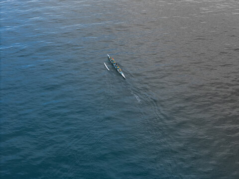 Aerial view of a long outrigger canoe with people paddling across the deep blue ocean water Wrightsville Beach, North Carolina, United States.