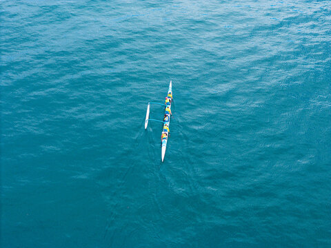 Aerial view of an outrigger canoe with people paddling across the blue ocean water at Wrightsville Beach, North Carolina, United States.