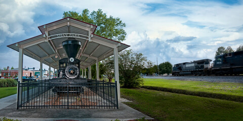 Vintage steam locomotive display beside a passing freight train in a Mississippi park © BJ Ray