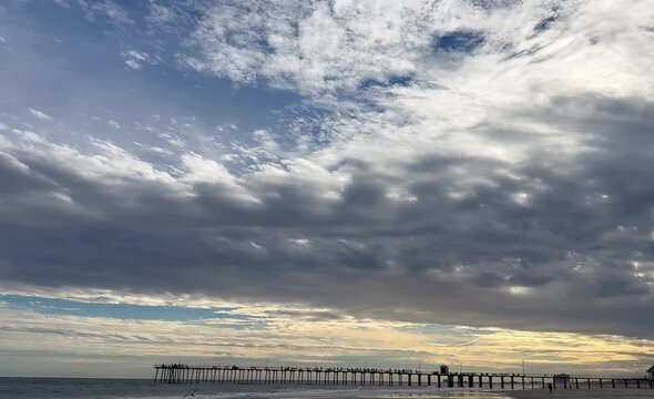 Down tilt dramatic cloud sky to pier, beach and ocean