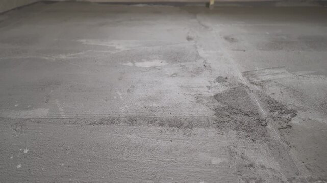 Tracking shot over a newly laid cement screed. Close up view of a gray, textured, self leveling compound on a concrete floor at a construction site. Industrial background for renovation or building