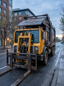 yellow garbage truck with installed front loader of fork type stands on city street in front of building specialized heavy machinery for performing loading and municipal works