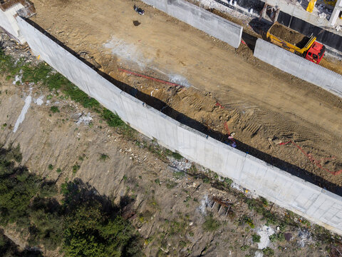 Aerial view of a construction site featuring a long concrete retaining wall, excavated earth, and a dump truck in Istanbul, Istanbul, Turkiye.
