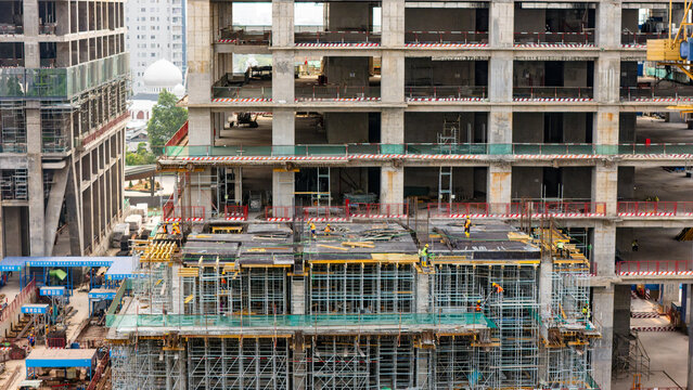 Aerial view of a high-rise building under construction with scaffolding and workers in yellow hard hats working on the concrete structure in Jakarta, Indonesia.