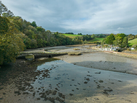 Aerial view of the historic stone Terras Bridge spanning the tidal East Looe River, surrounded by lush green hills, mudflats, and dense woodland in Looe, Cornwall, United Kingdom.