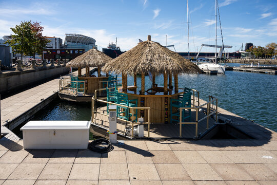 Cleveland, Ohio, United States - 08 October 2026: View of tiki bars on a floating dock in the harbor with sailboats and a stadium in the background.