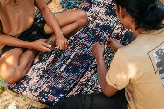 Waingapu, Indonesia - 01 August 2026: View of two men working at an ikat factory, carefully adjusting intricate threads on a traditional loom with small tools.