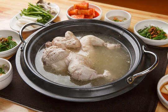 Whole chicken soup boiling in black pot served with assorted korean side dishes