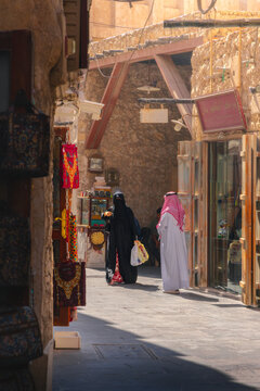 Doha, Doha Municipality, Qatar - 09 November 2025: View of Souq Waqif with a woman in a black abaya and a man in a white thobe walking through the historic market alleyway.