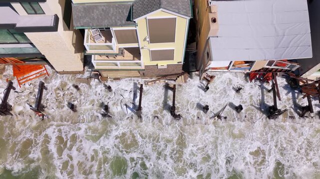 Long Beach, California, USA - October 15, 2026: Top down flight left to right over surf washing through splintered boardwalk, broken pilings and damaged homes after Tropical Storm Rachel.