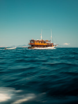 Komodo, East Nusa Tenggara, Indonesia - 26 July 2026: View of a wooden phinisi boat sailing on the sea near Komodo National Park with a small tender boat trailing behind under a clear sky.