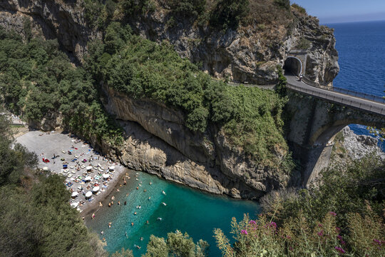 Amalfi, Italy - 14 October 2026: View of Fiordo di Furore with its iconic stone bridge, turquoise waters, and sunbathers on the pebble beach under a clear sky.