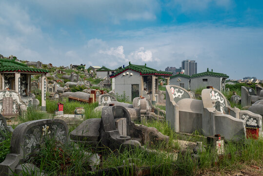 Tainan, Taiwan - 12 May 2015: View of traditional Chinese-style tombs with green tiled roofs and stone markers in a grassy cemetery under a blue sky.
