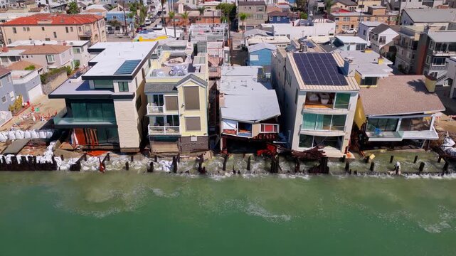 Long Beach, California, USA - October 15, 2026: Flight right to left as waves crash through broken pilings and sandbags into sagging, collapsed homes on the Peninsula after Tropical Storm Rachel.