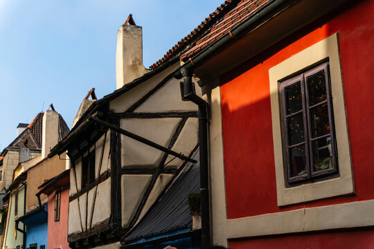 Prague, Prague, Czechia - 05 October 2026: View of colorful historic buildings featuring traditional half-timbered architecture and a vibrant red facade under a clear blue sky.