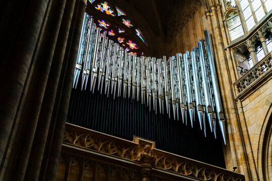 Prague, Czechia - 05 October 2026: View of the pipe organ inside St. Vitus Cathedral, featuring metal pipes set against ornate Gothic stone architecture and colorful stained glass.